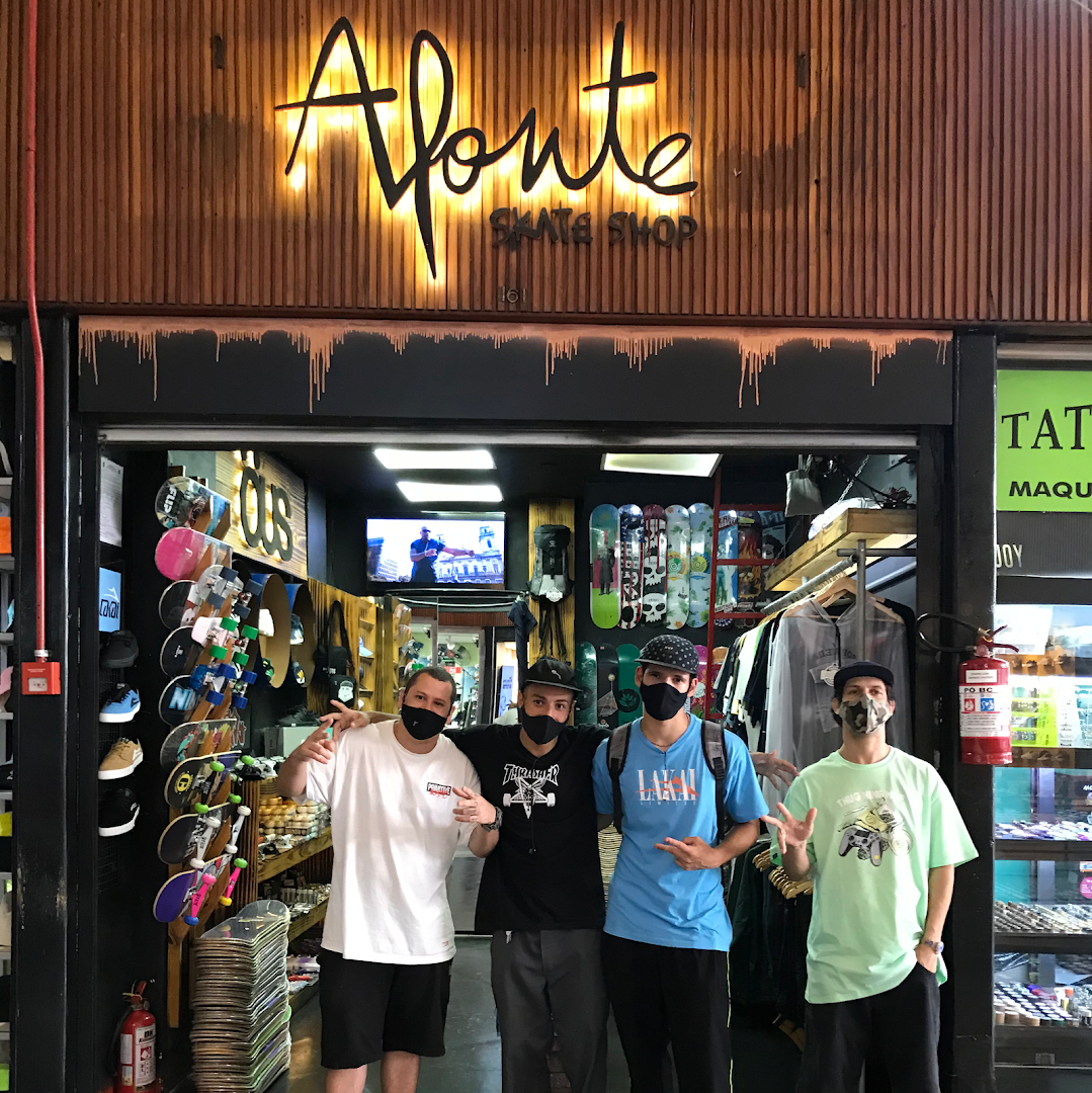 Four people stand in front of a skate shop with skateboards and apparel displayed inside.