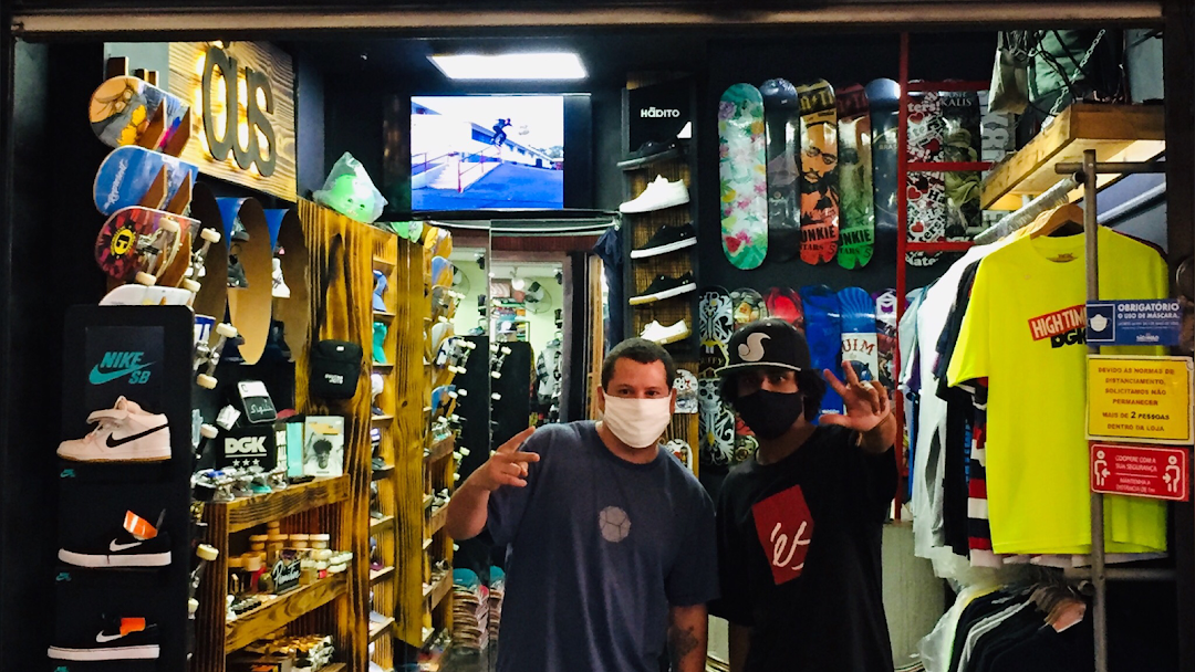 Two people wearing masks stand inside a skate shop filled with skateboards and apparel.
