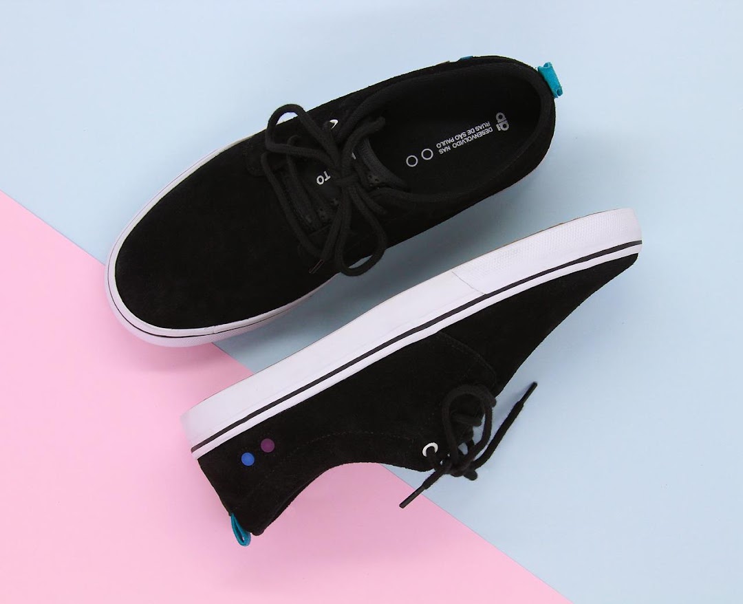 A pair of black suede sneakers with white soles and laces, displayed on a pastel background.