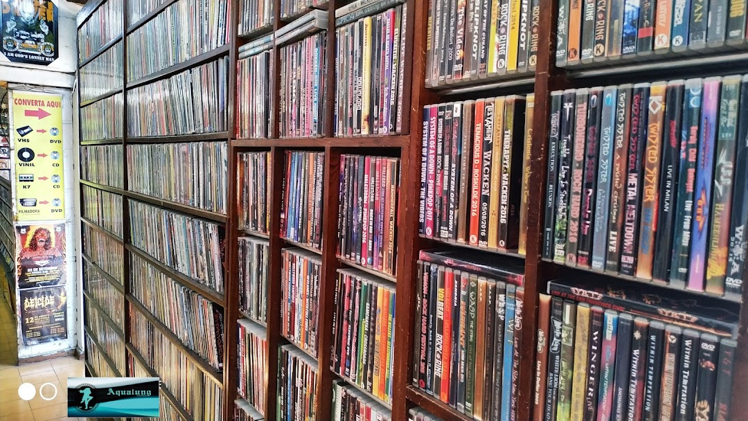 A shop interior filled with shelves packed with DVDs and CDs, featuring band posters on the wall.
