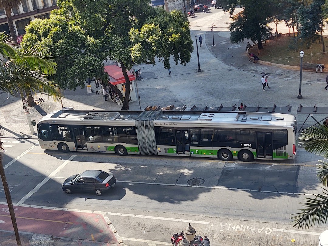 A long articulated bus is driving on a city street with a car behind it.