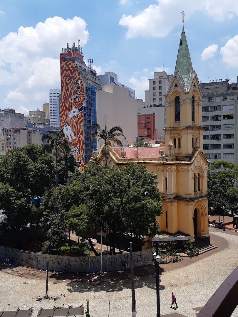 A yellow church with a green spire stands next to a building with a colorful mural.