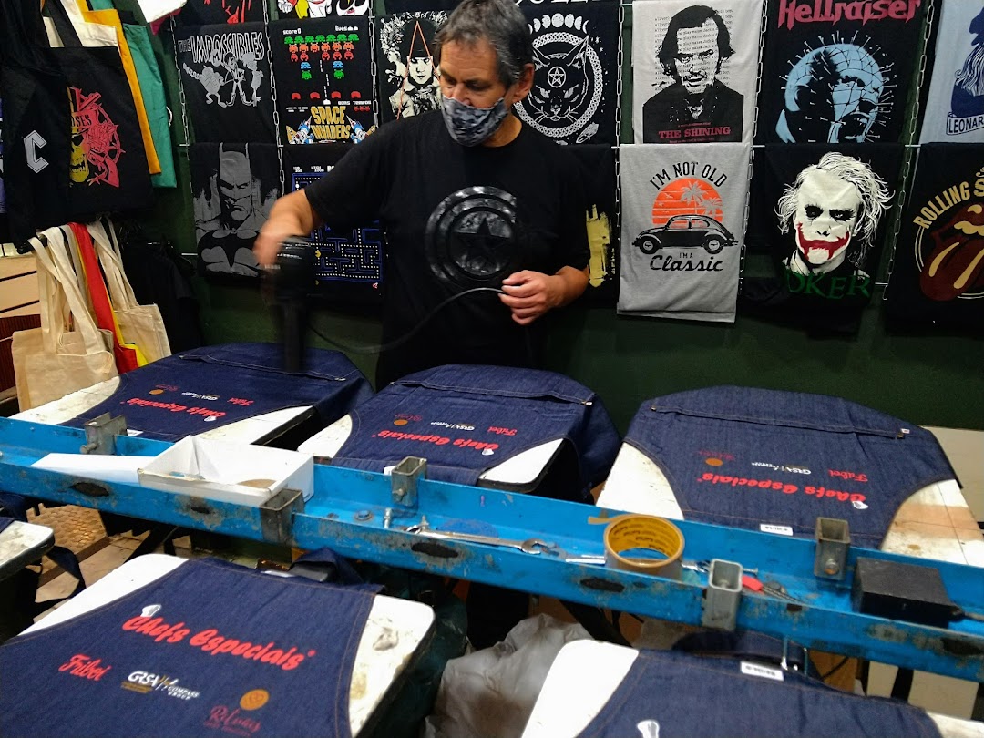 A man is using a heat gun on custom printed aprons at a t-shirt printing shop.