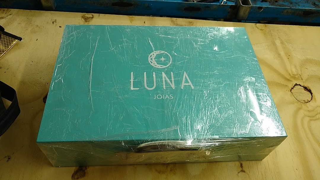A teal jewelry box with the Luna Joias logo, wrapped in plastic.