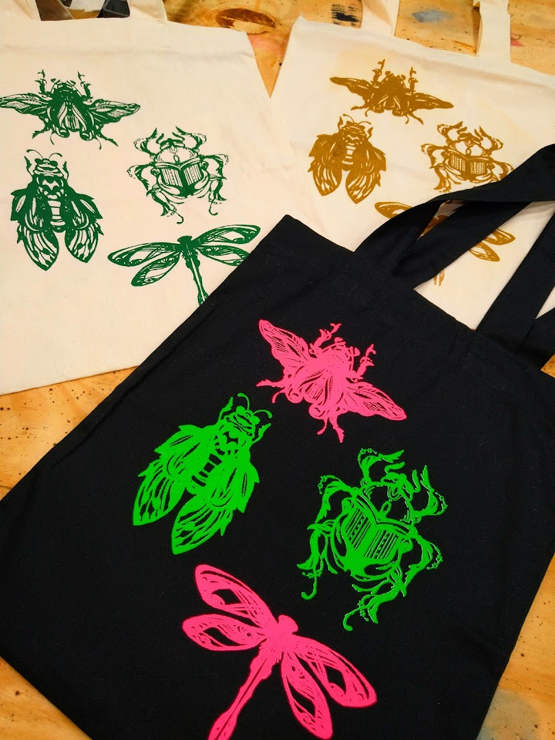 Tote bags with vibrant insect prints in green, pink, and gold.