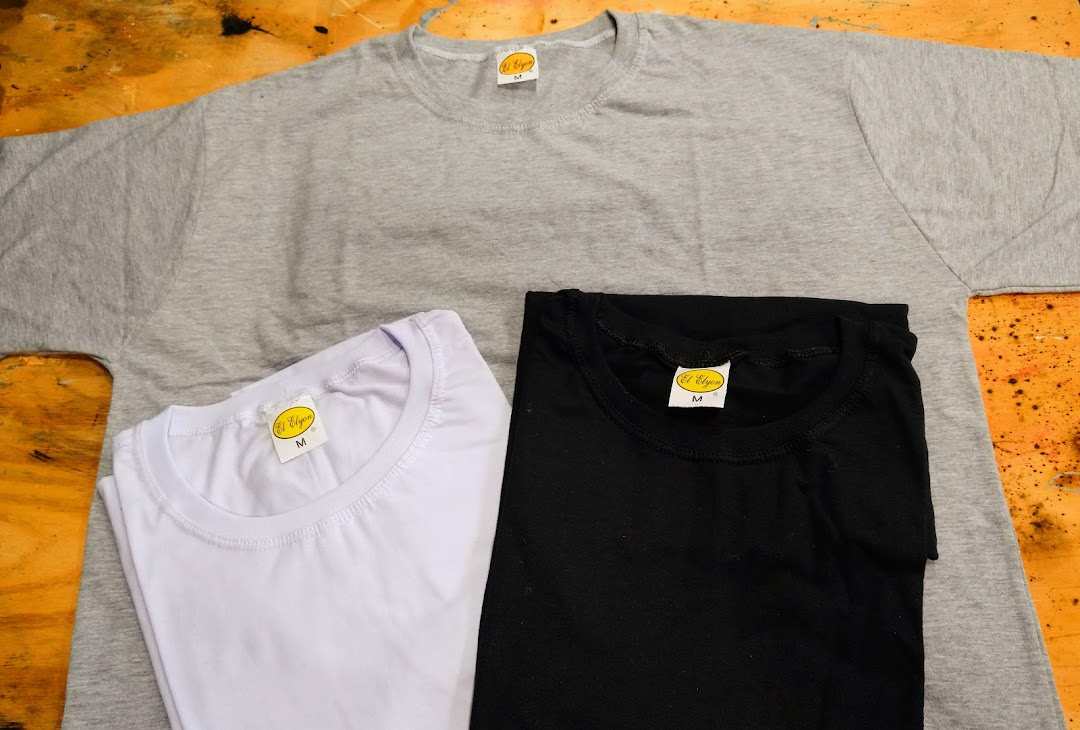 Three plain t-shirts in grey, white, and black are laid out on a wooden surface.