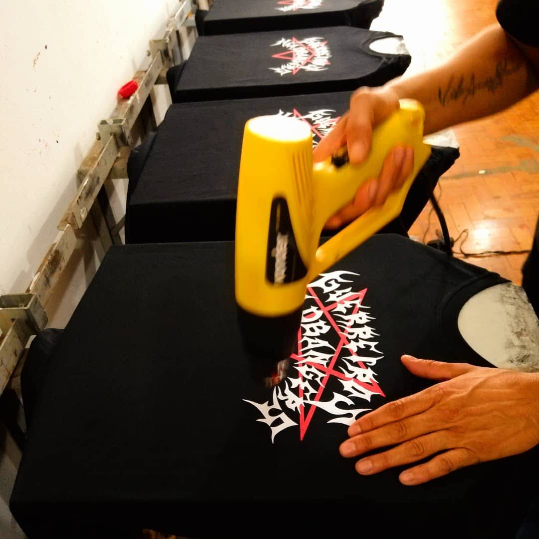 A person uses a heat gun to apply a graphic design onto a black t-shirt.