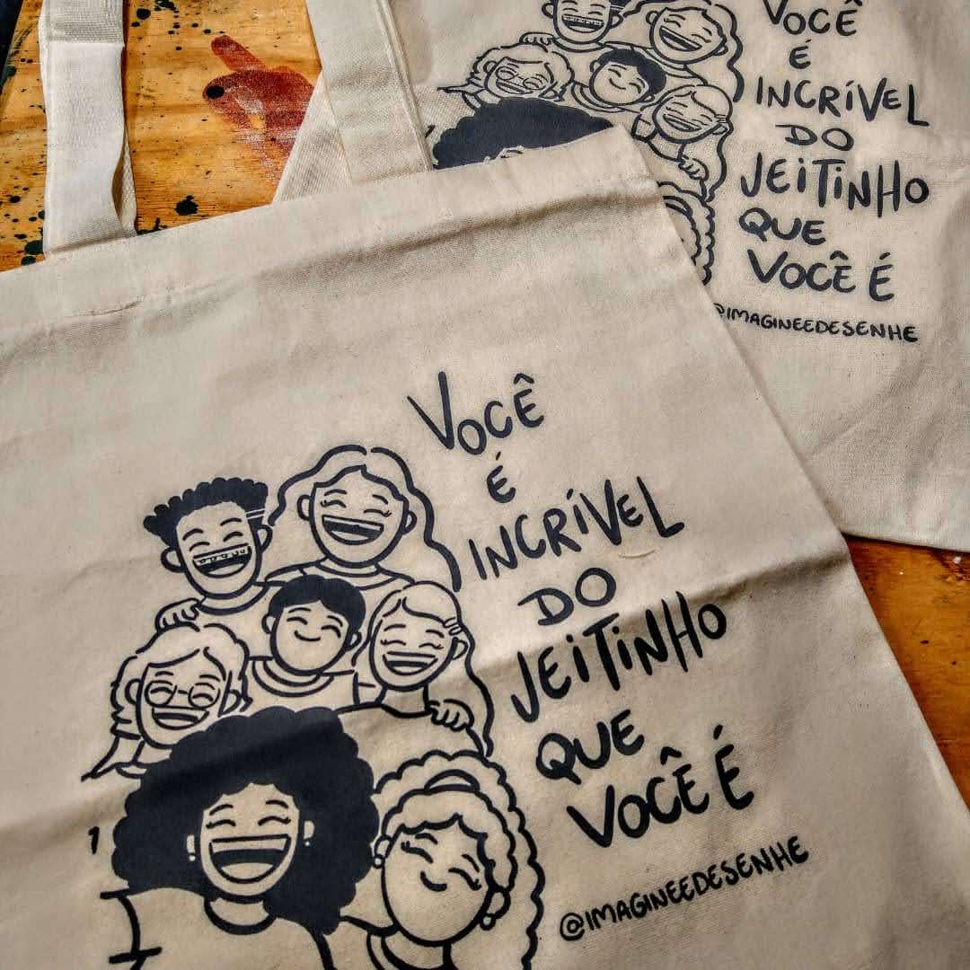 Two canvas tote bags with a black ink illustration of smiling people and empowering text.