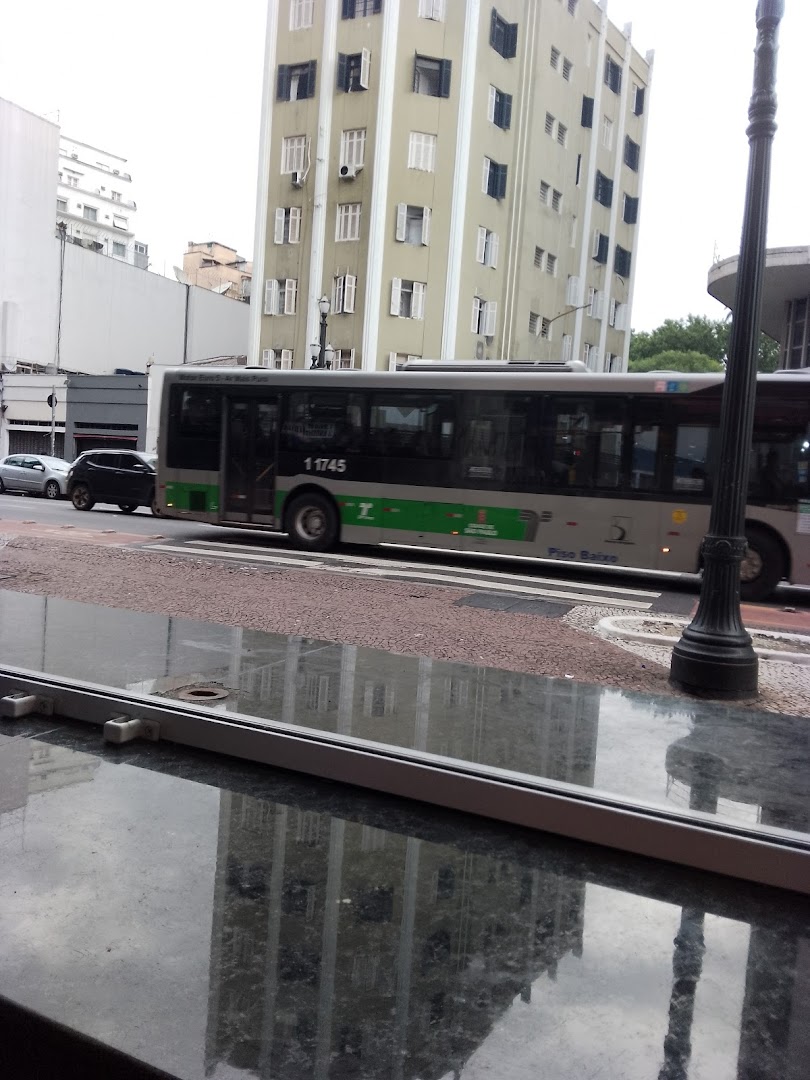 A bus passes by a tall building with many windows, reflected in a wet surface.