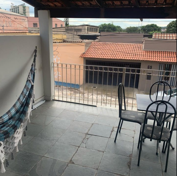 A balcony with a hammock and a small table with chairs overlooking a street.