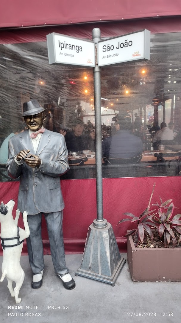 A statue of a man and dog stands outside a restaurant with street signs.