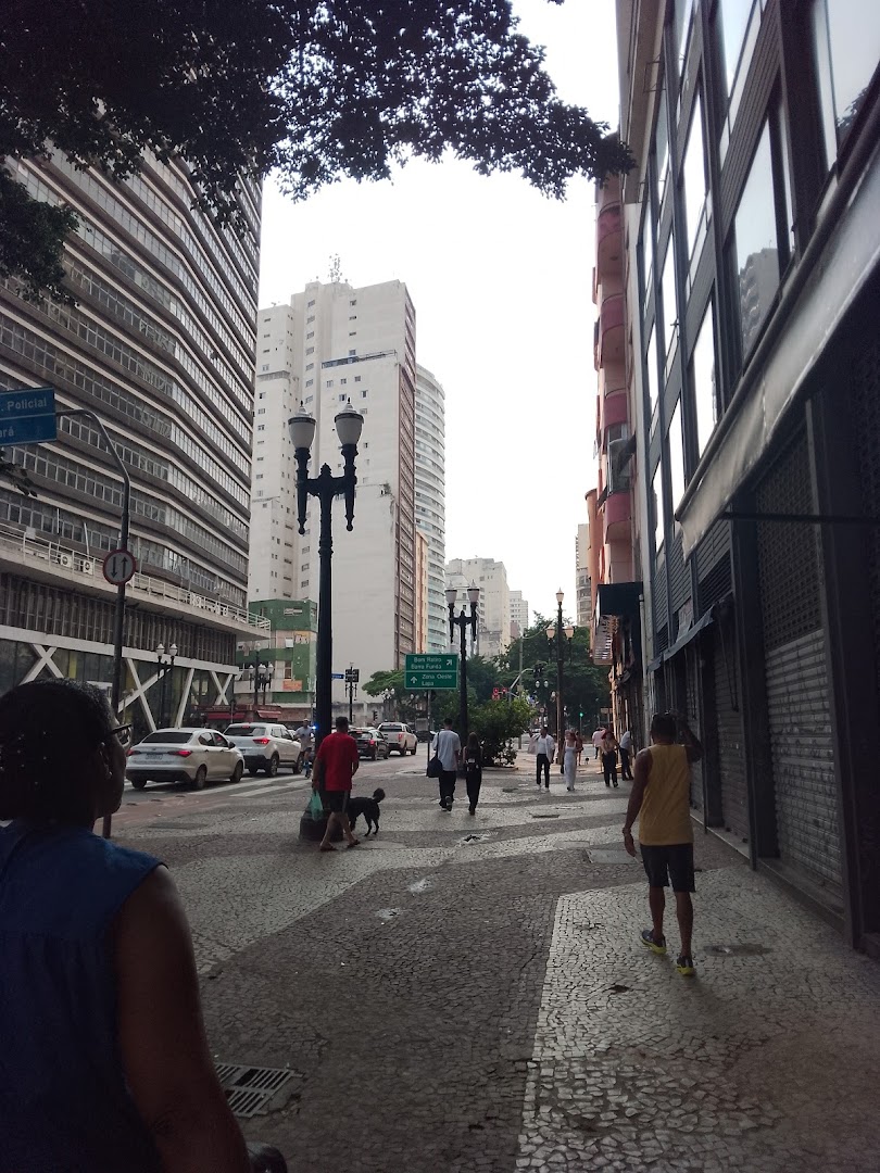 People walking on a city sidewalk with buildings and traffic in the background.