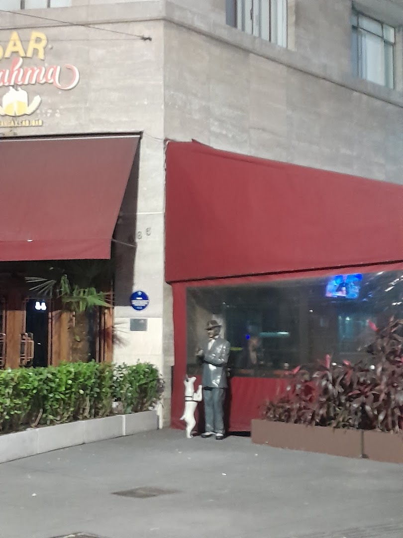 A statue of a man with a dog stands outside a bar with red awnings.
