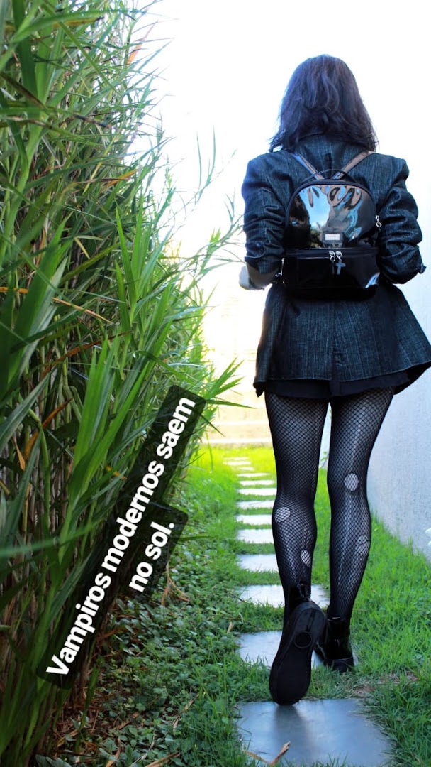 A person in stylish gothic attire walks down a garden path.