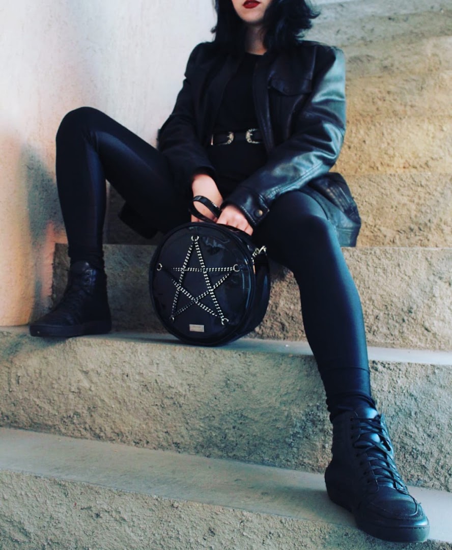 A person in black clothing sits on concrete steps, holding a circular bag with a star design.