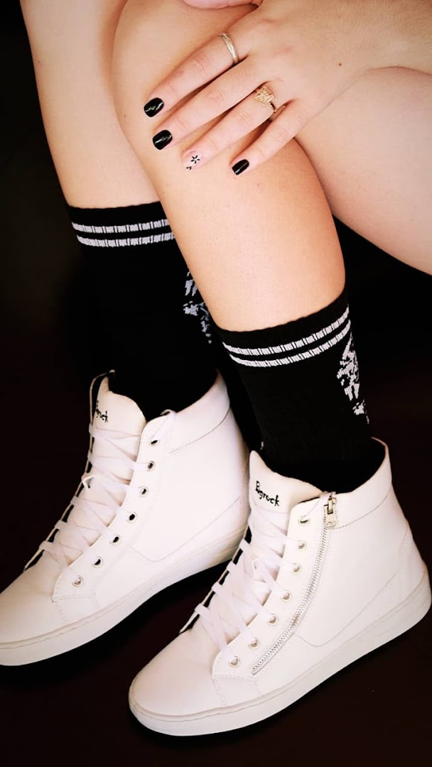 A person wearing white high-top sneakers and black socks with white stripes.