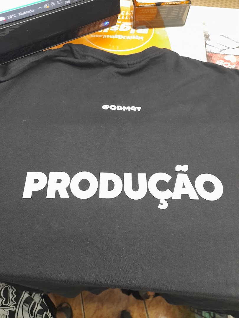 A black t-shirt with white text "PRODUÇÃO" and "@ODMGT" printed on it.