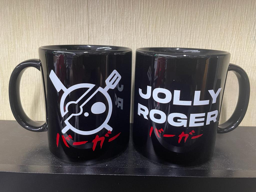 Two black mugs with white and red designs, one featuring a Jolly Roger skull and the other text.