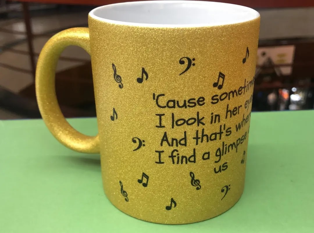 A gold glitter mug with musical notes and lyrics printed on it.