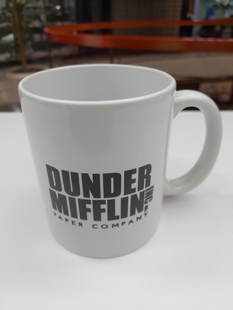 A white mug with the Dunder Mifflin Paper Company logo is displayed.