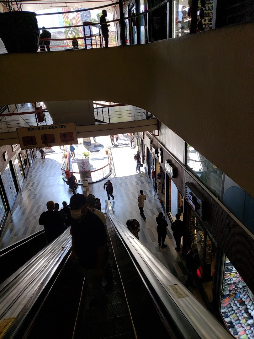 People on escalators in a multi-level shopping mall with shops visible.