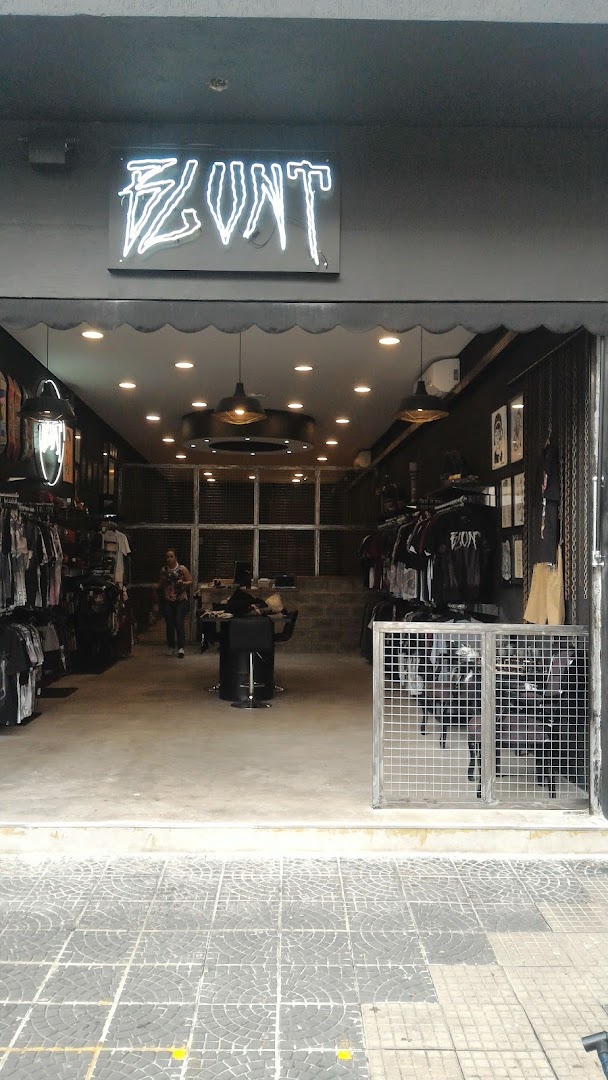 The entrance of Blunt Brasil, a clothing store with a neon sign and racks of apparel.