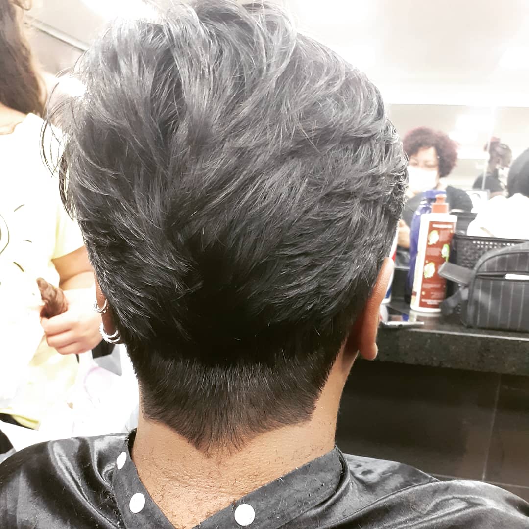 A person's head from behind, showing a fresh haircut and a stylist in the background.