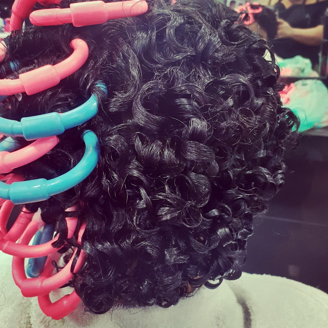 Close-up of dark curly hair being permed with pink and blue rollers.