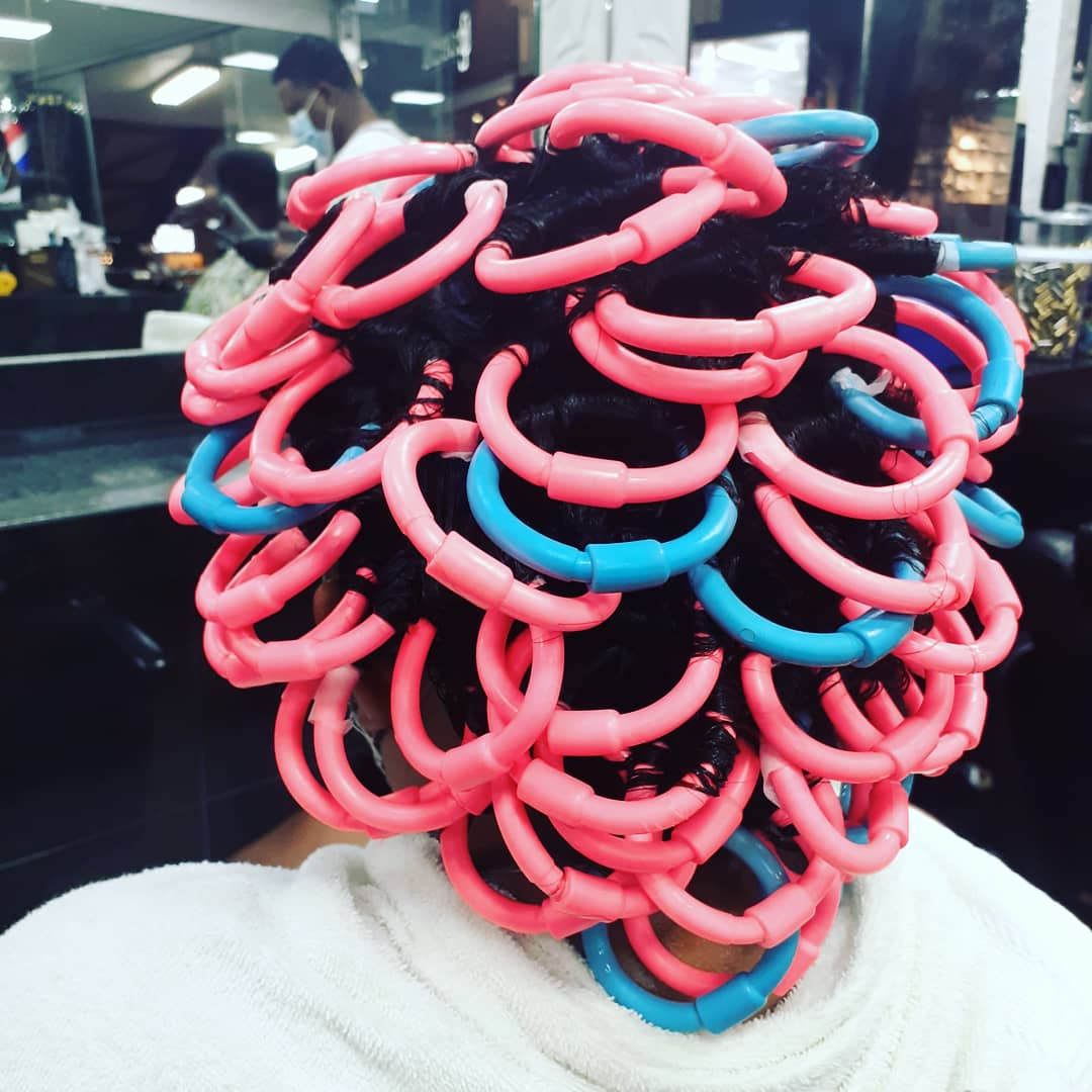 A person's head with dark hair styled using pink and blue perm rods.