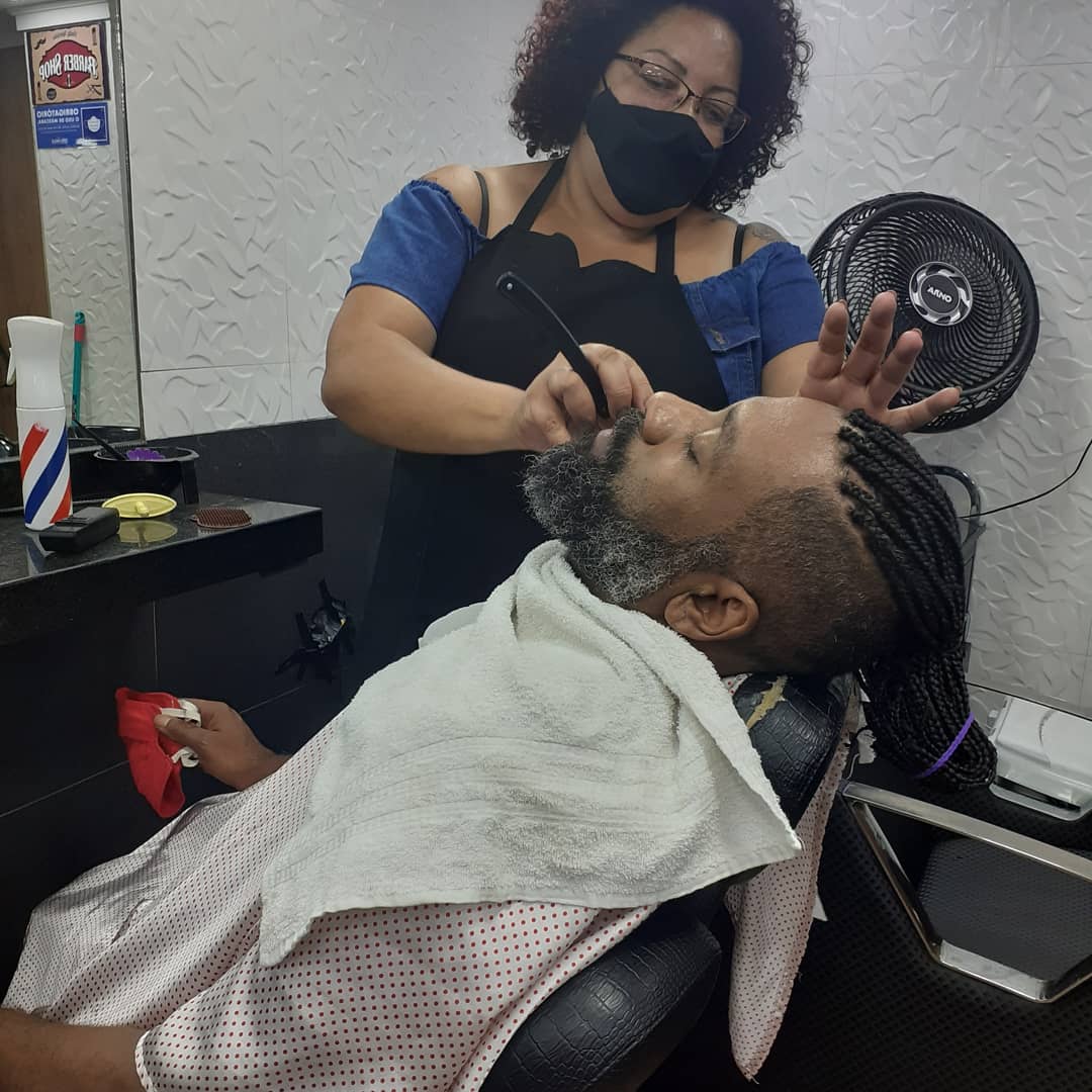 A barber is shaving a client's beard in a salon.