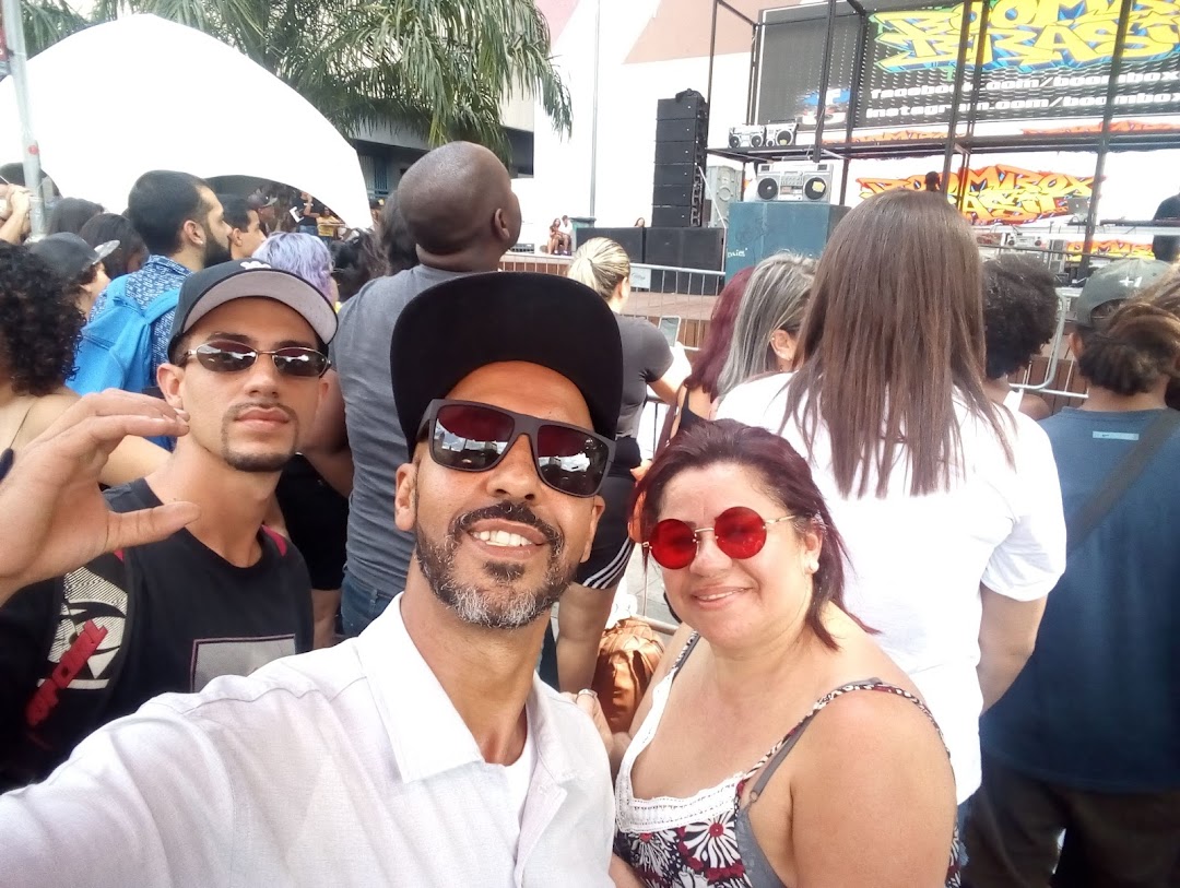 Two people taking a selfie in front of a crowd at an outdoor event with a stage.