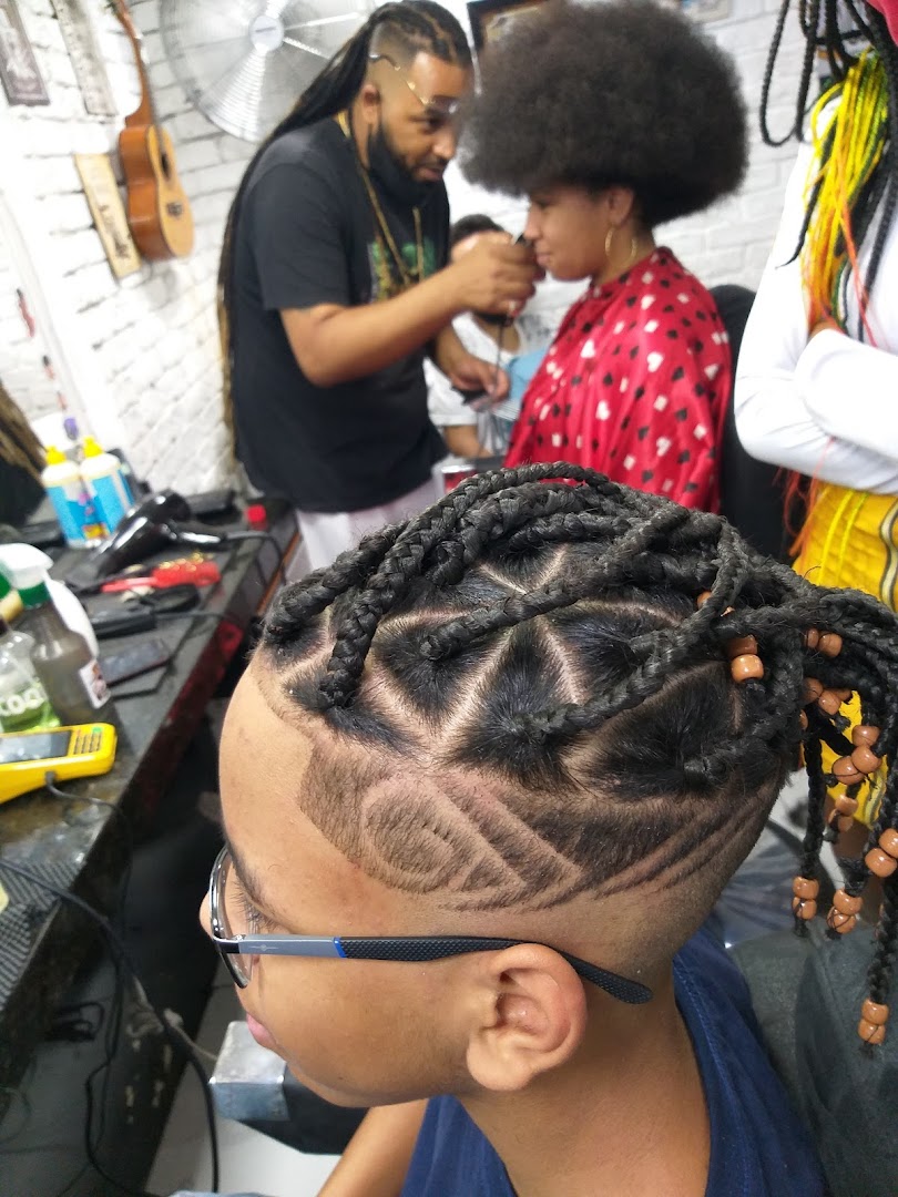 A barber styles a young person's hair with intricate braids and designs.