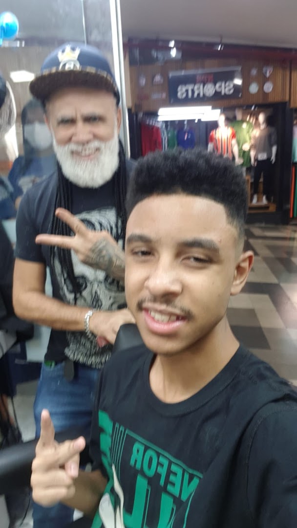 A barber with a white beard and a young man pose for a selfie in a salon.