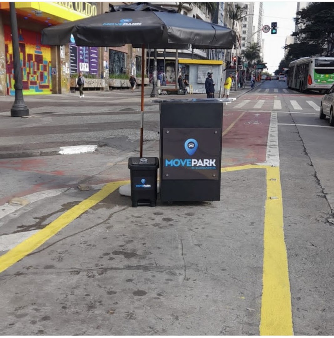 A Movepark valet parking station with an umbrella and trash can on a city street.