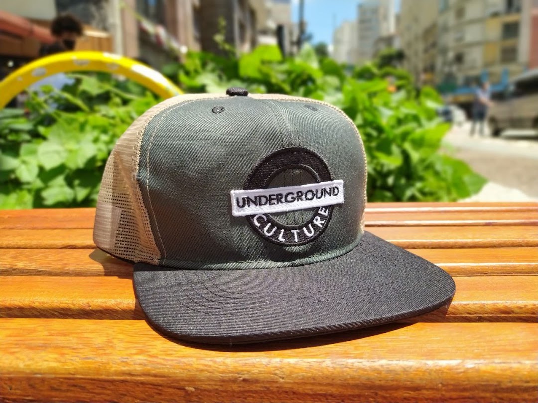 A close-up of a trucker hat with 'UNDERGROUND CULTURE' embroidered on it, resting on a wooden bench.