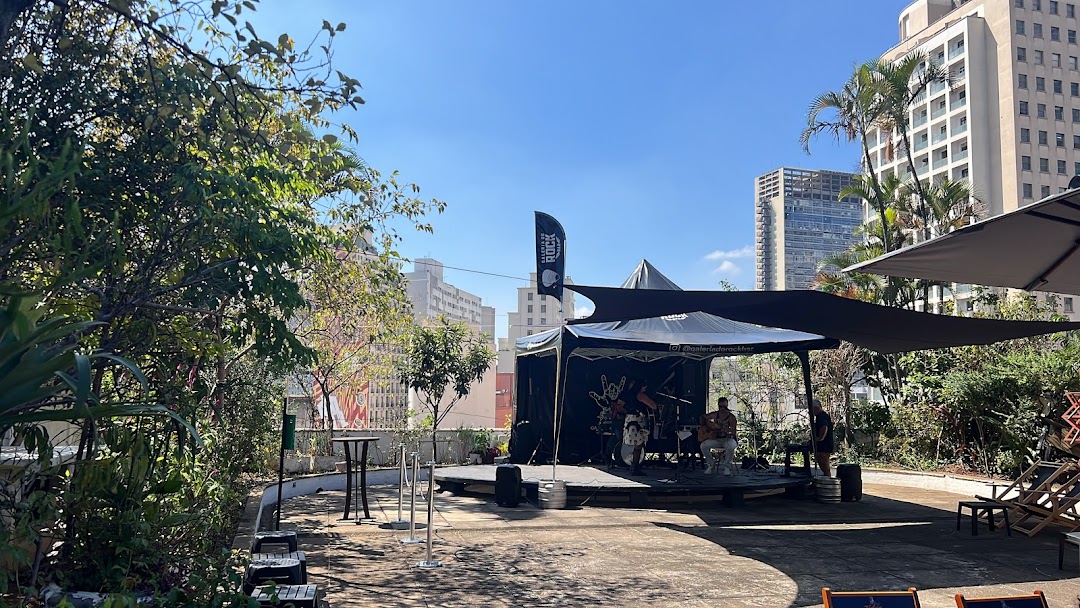 An outdoor stage with a band performing, set against a backdrop of city buildings and greenery.