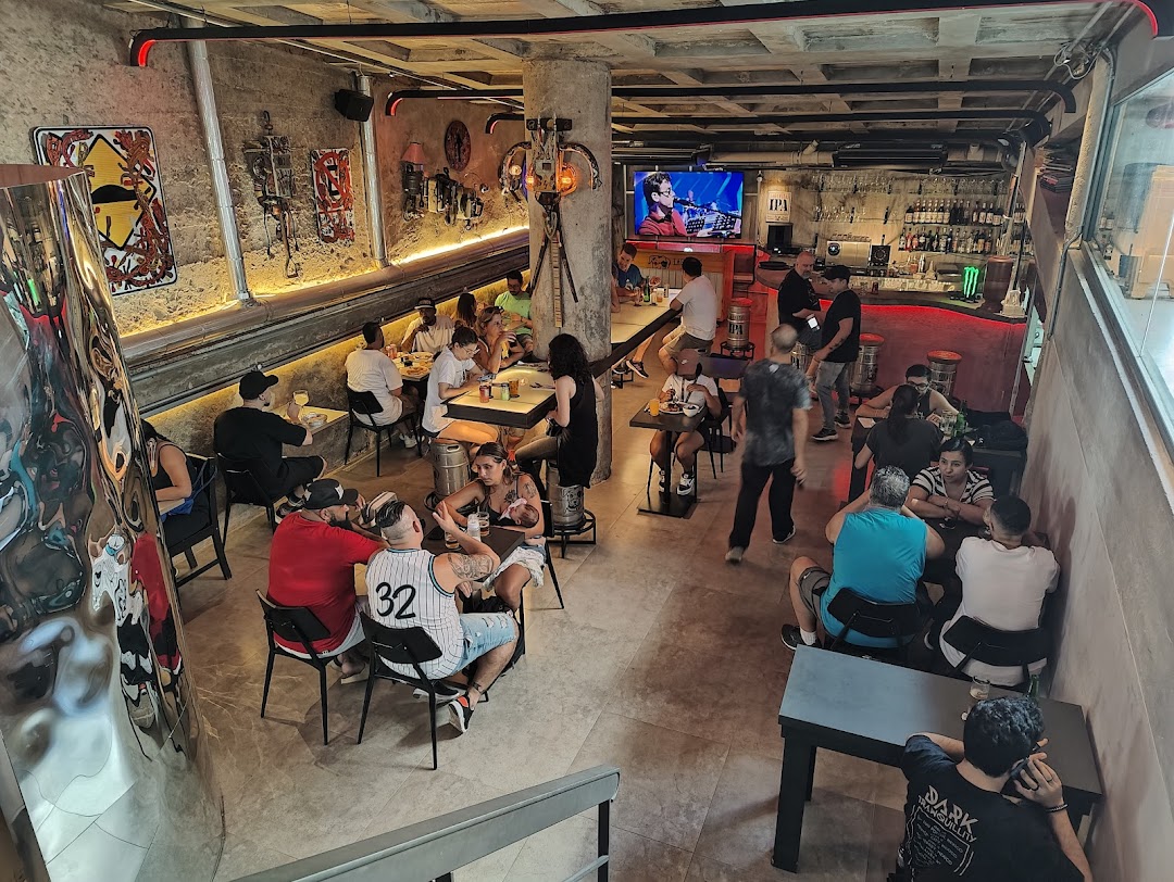 People enjoying drinks and food inside a lively bar with industrial-themed decor.