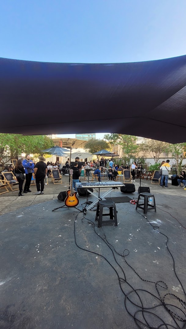 An outdoor venue with a stage, musical instruments, and people seated under umbrellas.