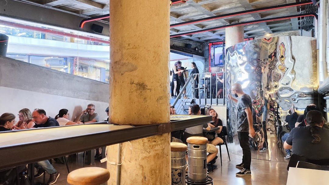 People sitting at tables inside a modern bar with industrial-style decor and a unique metallic wall.