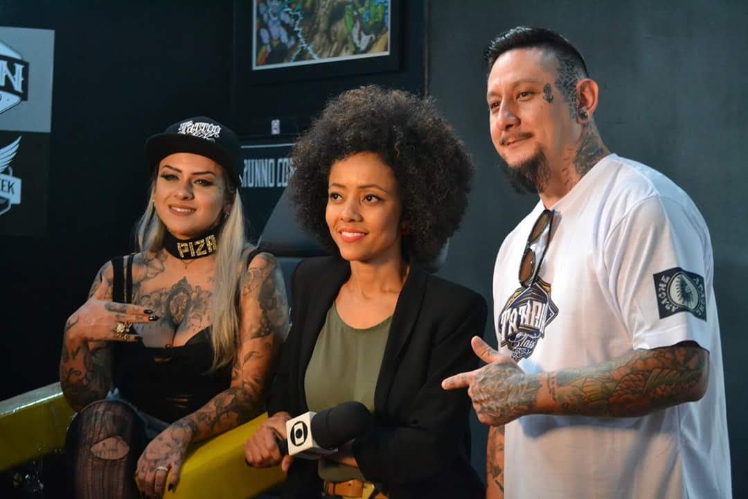 Three people, two women and one man, are posing for a photo in a tattoo studio.