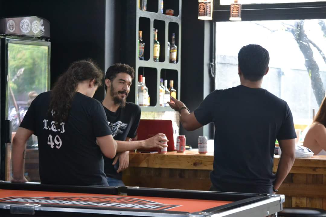 Three men are gathered around a bar, with a pool table in the foreground.