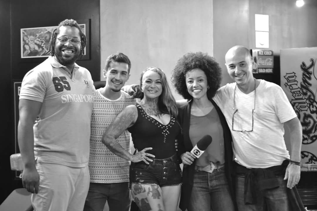 A group of five people, likely artists and a reporter, smiling for a photo inside a tattoo studio.