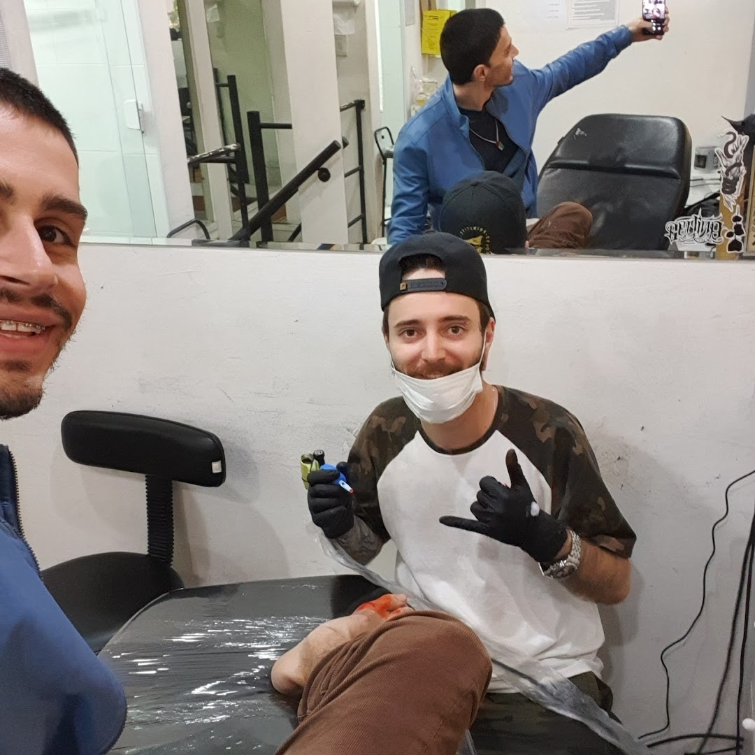 Tattoo artist with mask and gloves poses with client during a tattoo session.