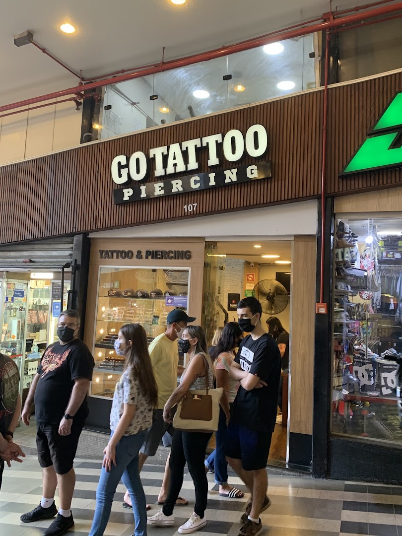 People walk past a tattoo and piercing shop with a prominent sign.