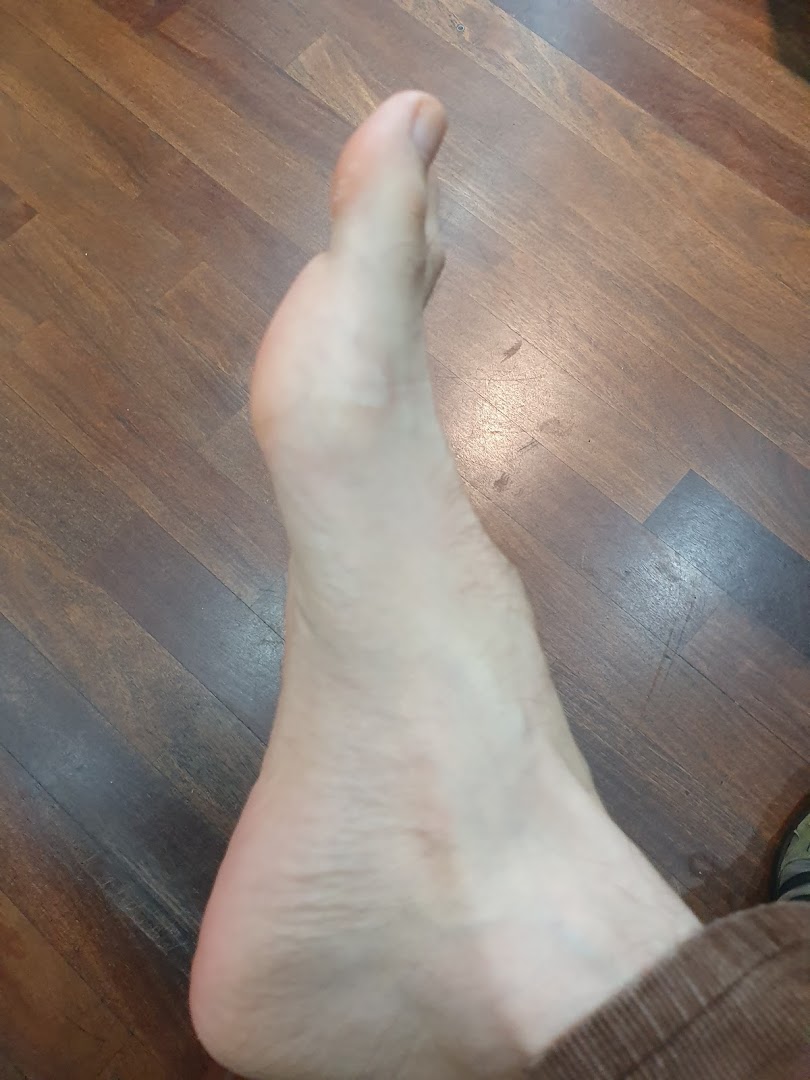A close-up shot of a bare foot resting on a wooden floor.