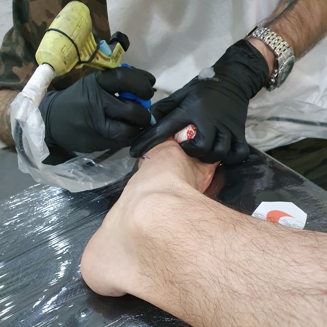 A tattoo artist is tattooing a foot with a tattoo machine and black gloves.