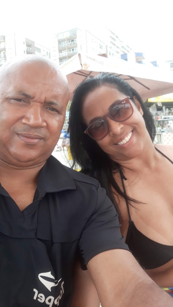 A couple smiles for a selfie at the beach with buildings in the background.