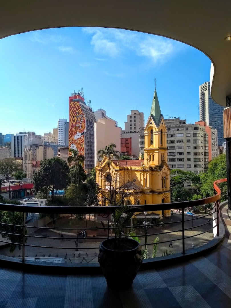 A view of a city skyline with a yellow church and modern buildings under a blue sky.