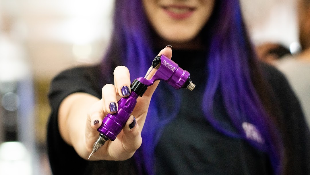 A person with purple hair holds a purple tattoo machine.