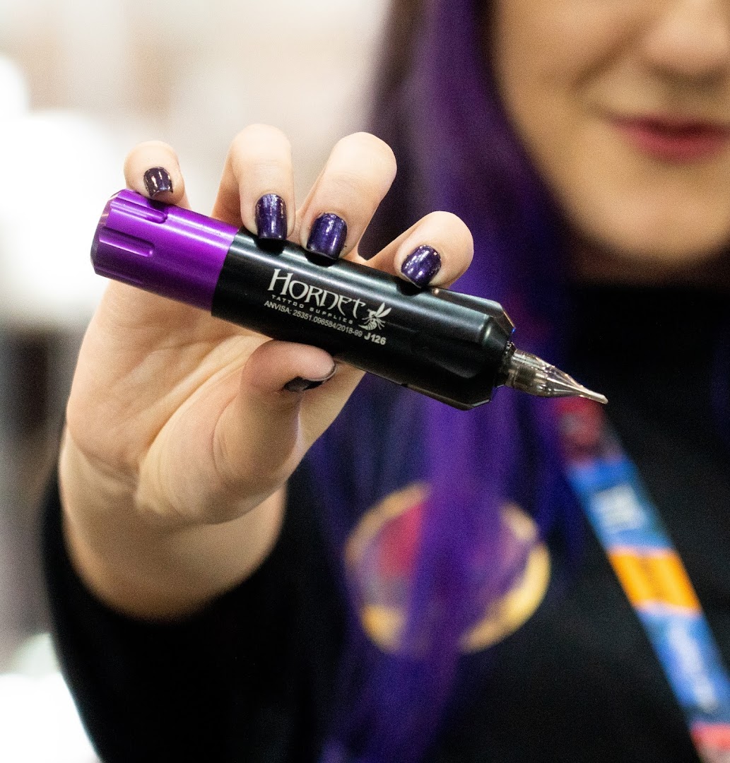 A person holds a purple and black tattoo machine with the brand name HORNET visible.